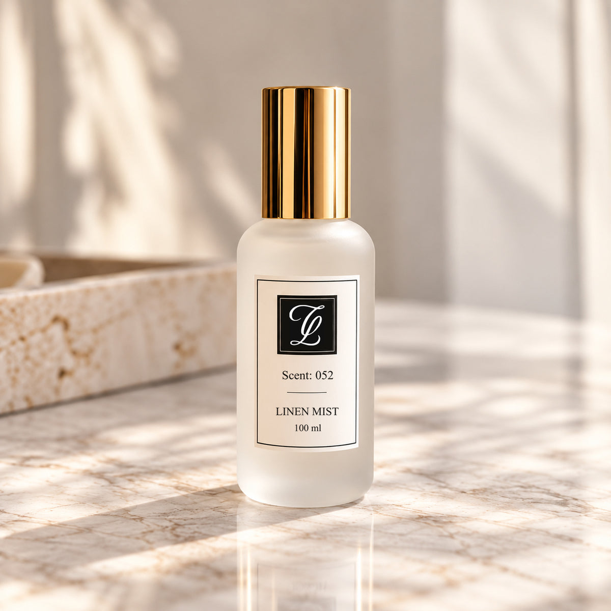Maison Fragrance Scent 052 Linen Mist, 100 ml, in a matte white bottle with a cylindrical gold cap and official CL monogram, on beige marble in soft natural light.
